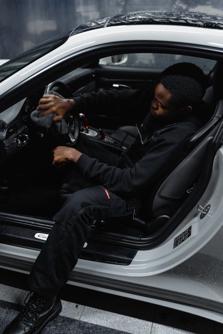 A Man Cleaning Steering Wheel Of A White Car