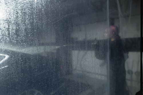 Free A person washes a car behind a water-streaked plastic curtain, creating a blurred effect. Stock Photo