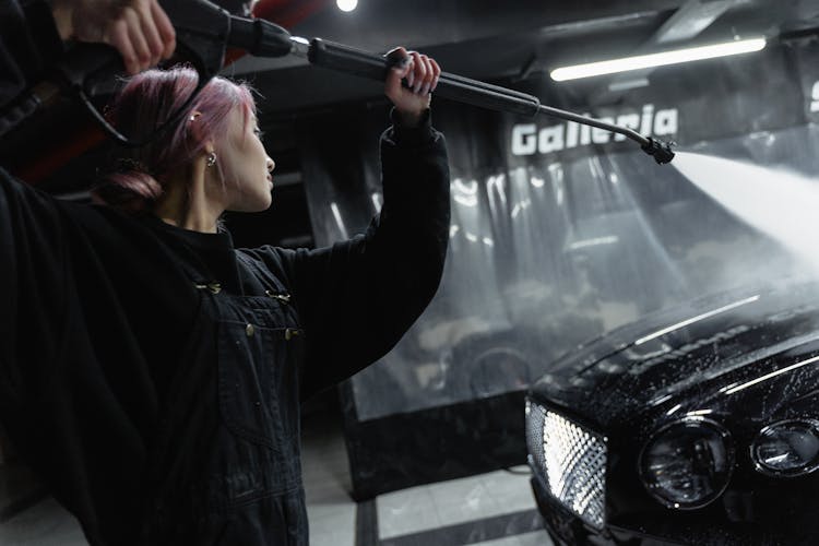 A Woman Washing A Car With A Power Spray