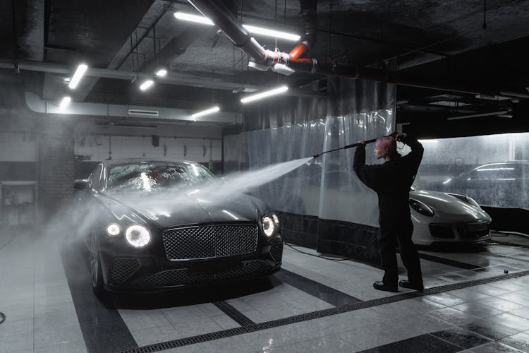 A Woman In Black Sweater Washing The Black Car Using Pressure Washer Hose