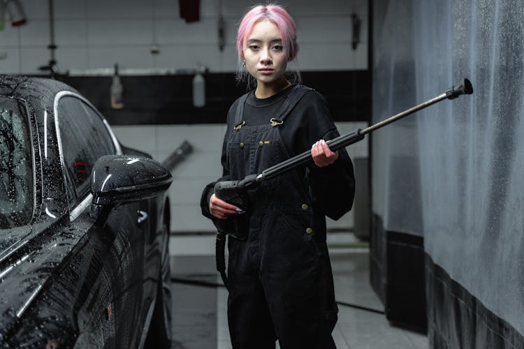 A Woman Holding A Pressure Washer Nozzle In A Car Wash