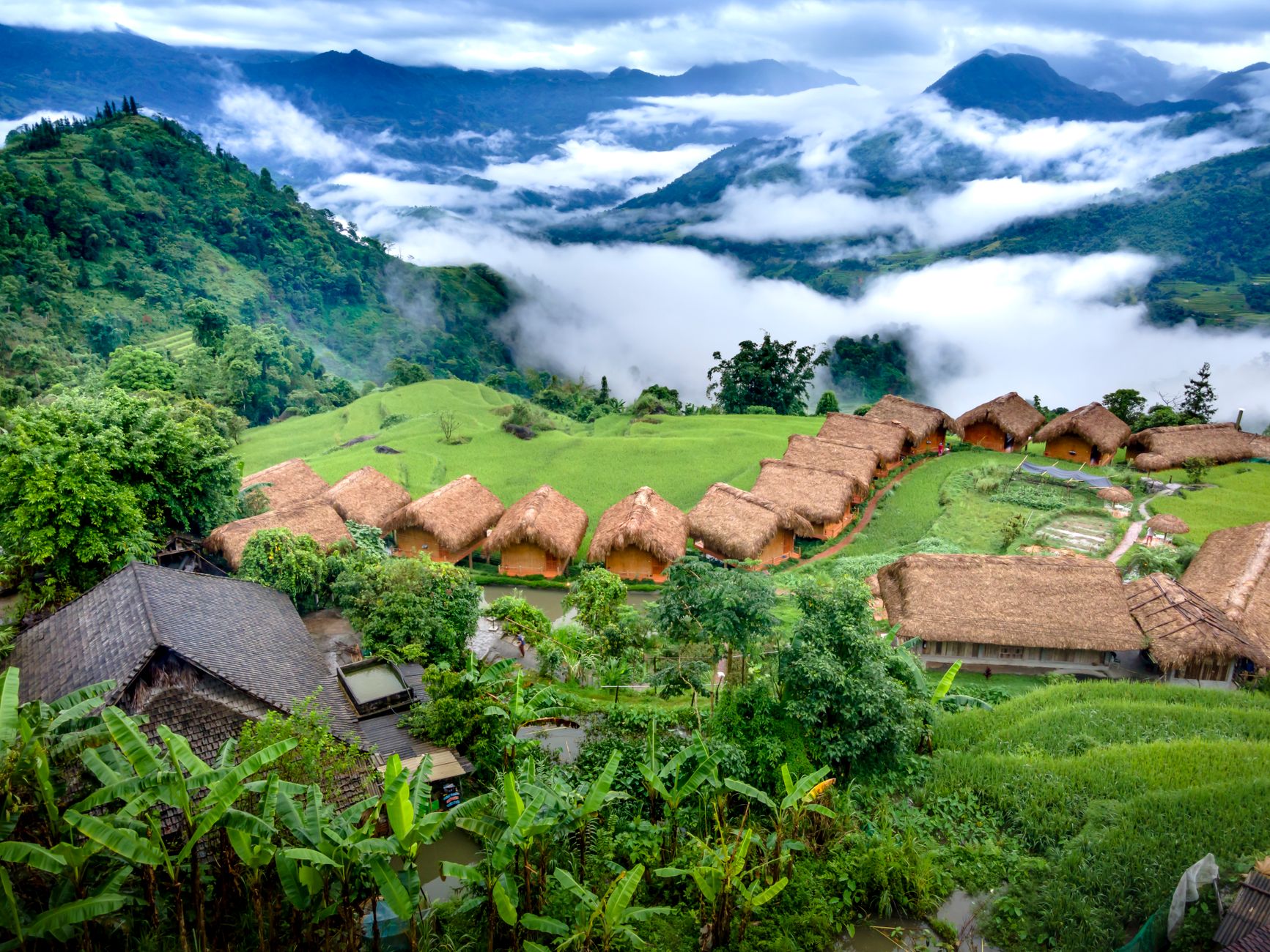 Breathtaking aerial shot of a traditional village nestled in misty mountains with lush greenery.