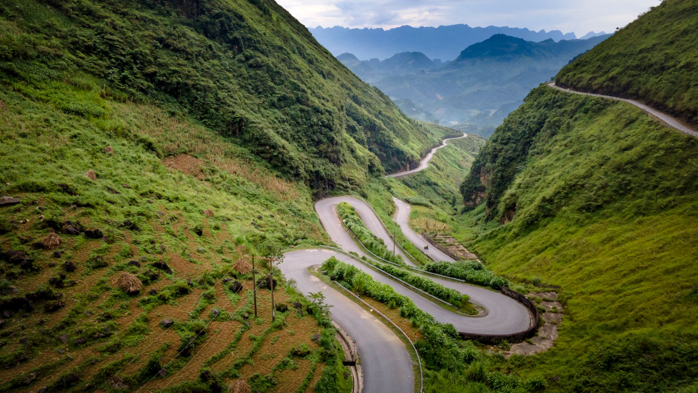 Scenic winding road through lush green mountains in serene natural landscape.