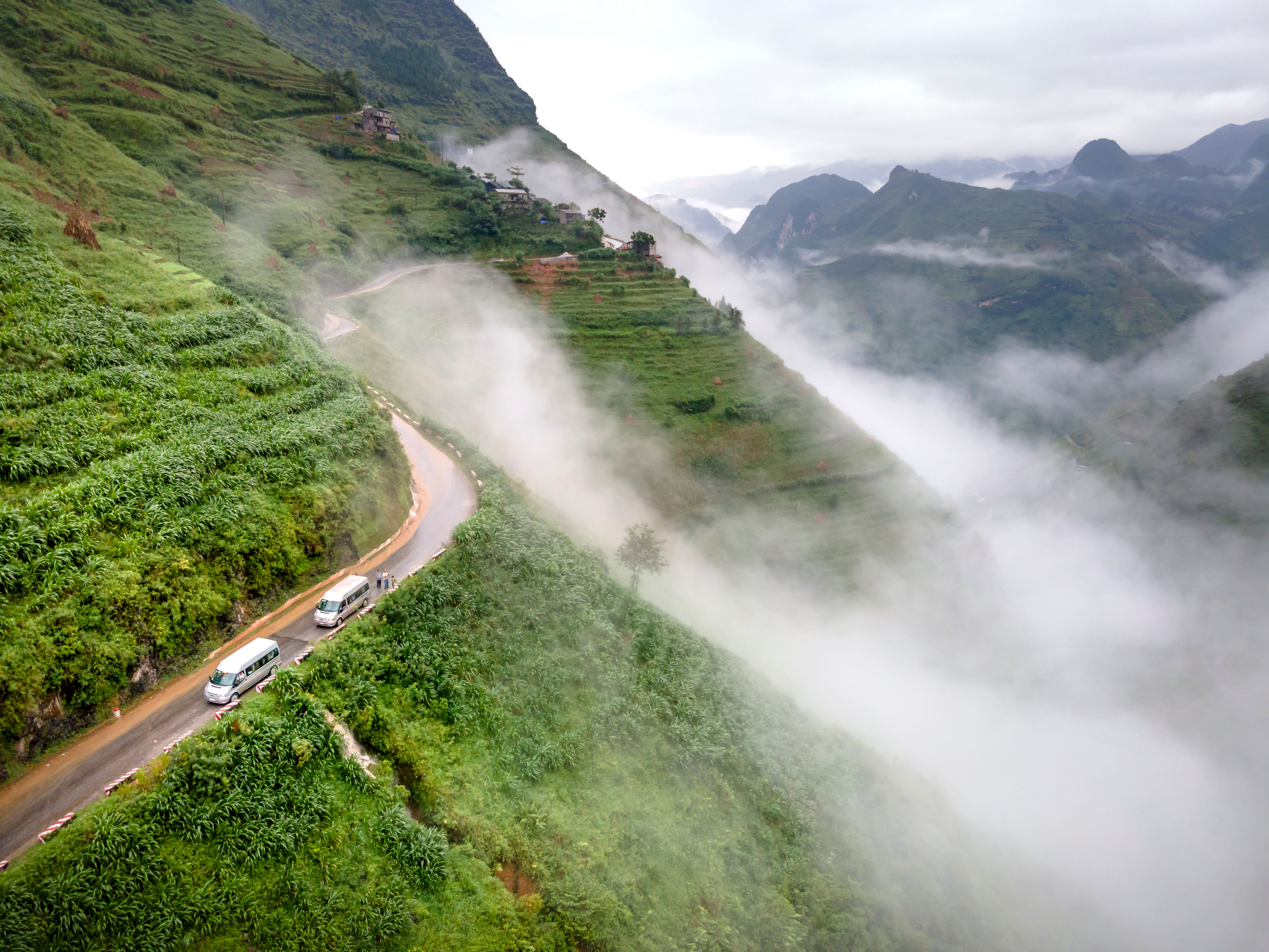 Breathtaking aerial shot of misty green mountains with a winding road and cars.