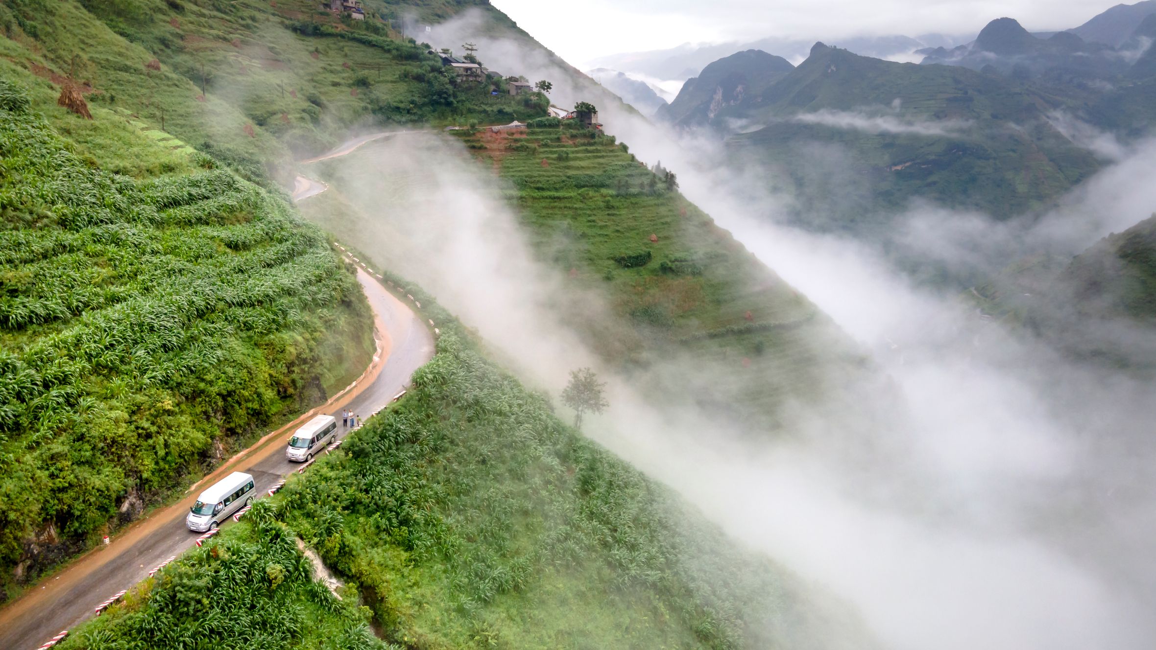 Breathtaking aerial shot of misty green mountains with a winding road and cars.