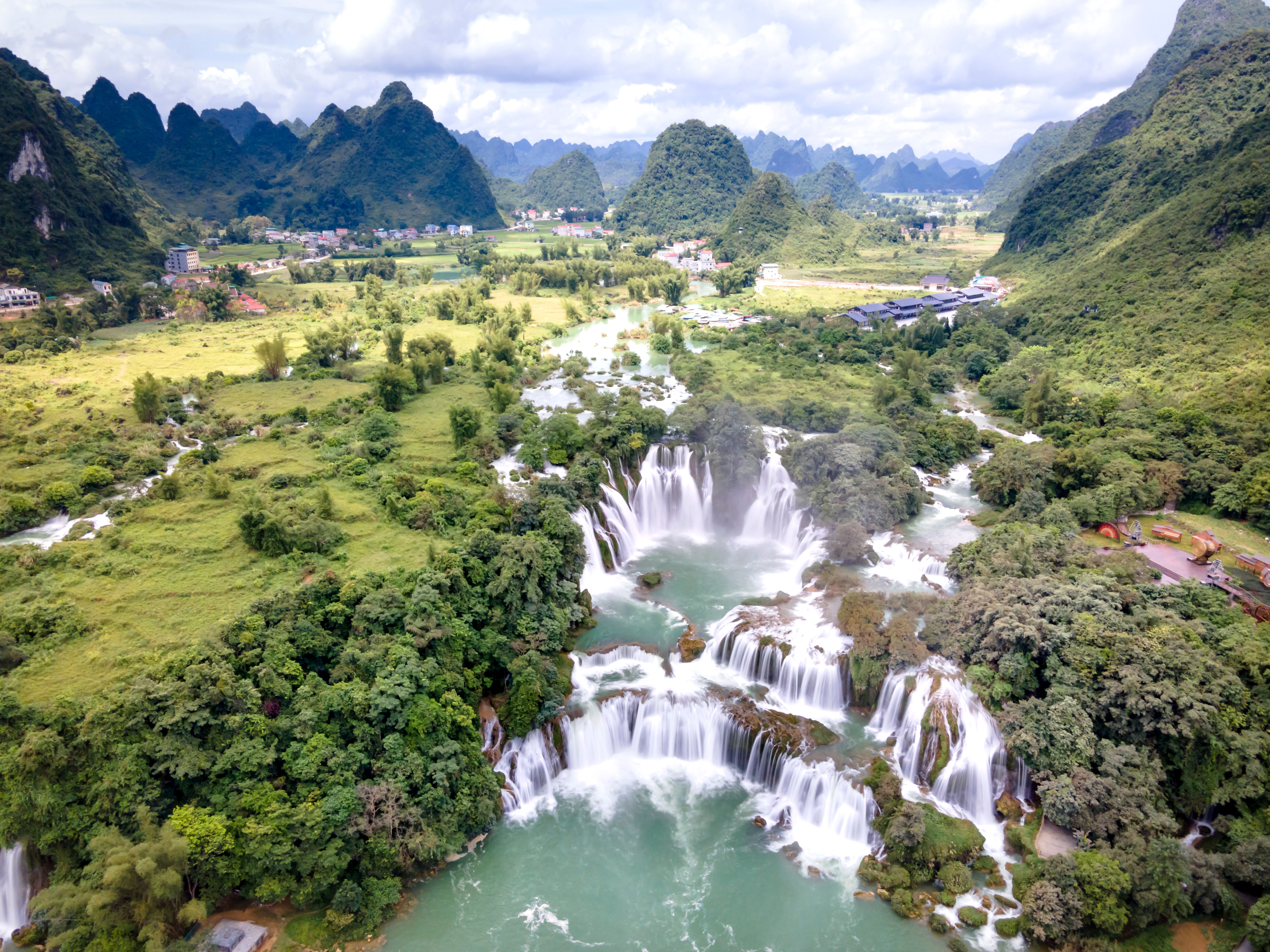 Stunning aerial view of a waterfall cascading through a lush green valley surrounded by mountains.
