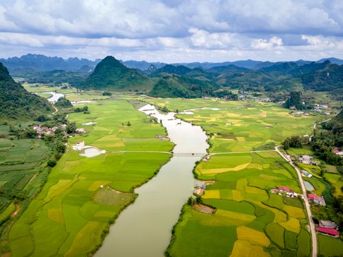 Free A stunning aerial photo showcasing lush green agricultural fields with a river cutting through and distant hills. Stock Photo