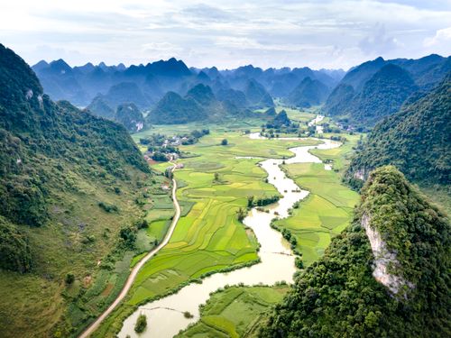 Free Stunning aerial photo of a green valley with winding river and hills under a cloudy sky. Stock Photo