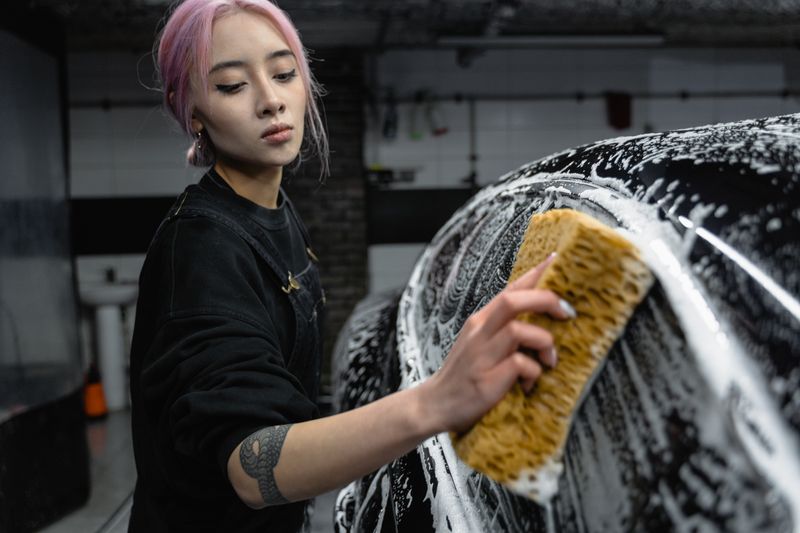 Detailer hand-washing a black car with sponge and soap
