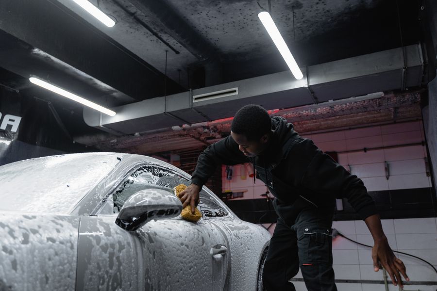 Worker hand-washing a car with a sponge and thick foam