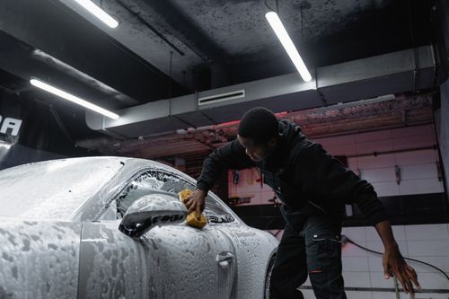 Free Man cleaning a car with soap and sponge at an indoor carwash facility. Stock Photo