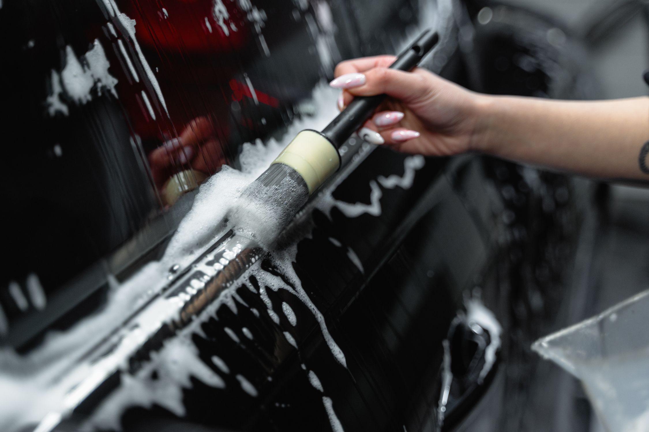 Close-up of a soft-bristle brush angled at 45 degrees against a blue truck panel with soapy water running down, demonstrating proper washing technique
