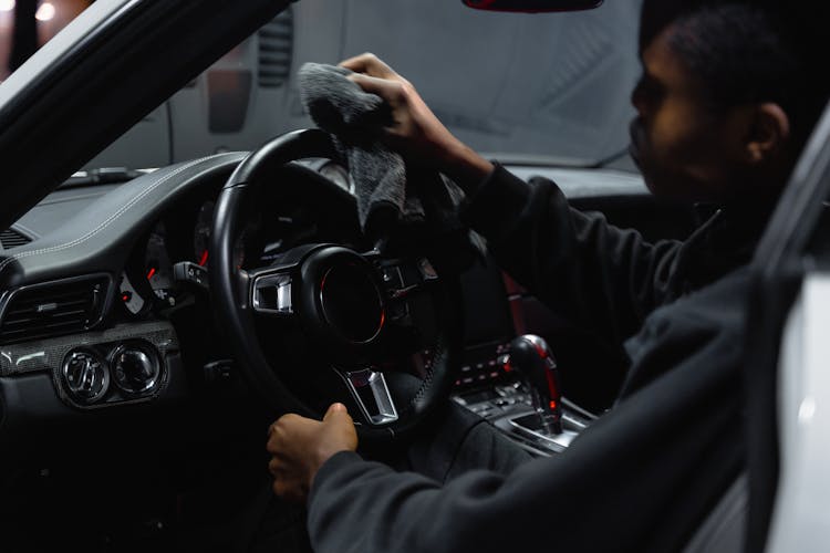 A Man In A Black Sweater Wiping The Steering Wheel Of A Car