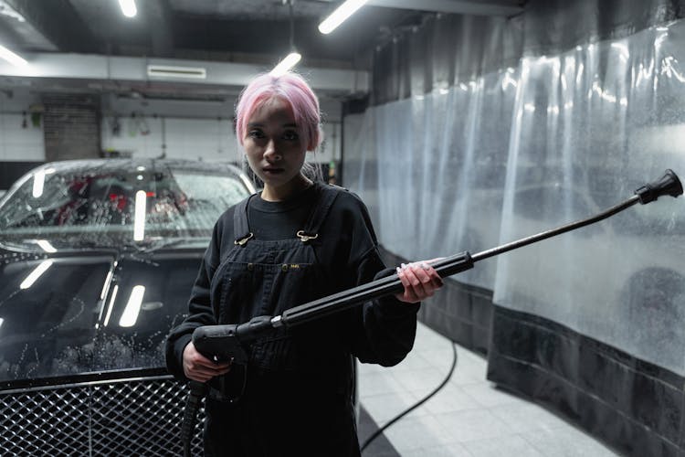 Woman With Pink Hair Looking At The Camera While Holding A Pressure Washer