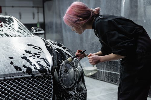 Free Photo of a Woman with Pink Hair Brushing the Headlight of a Black Car Stock Photo