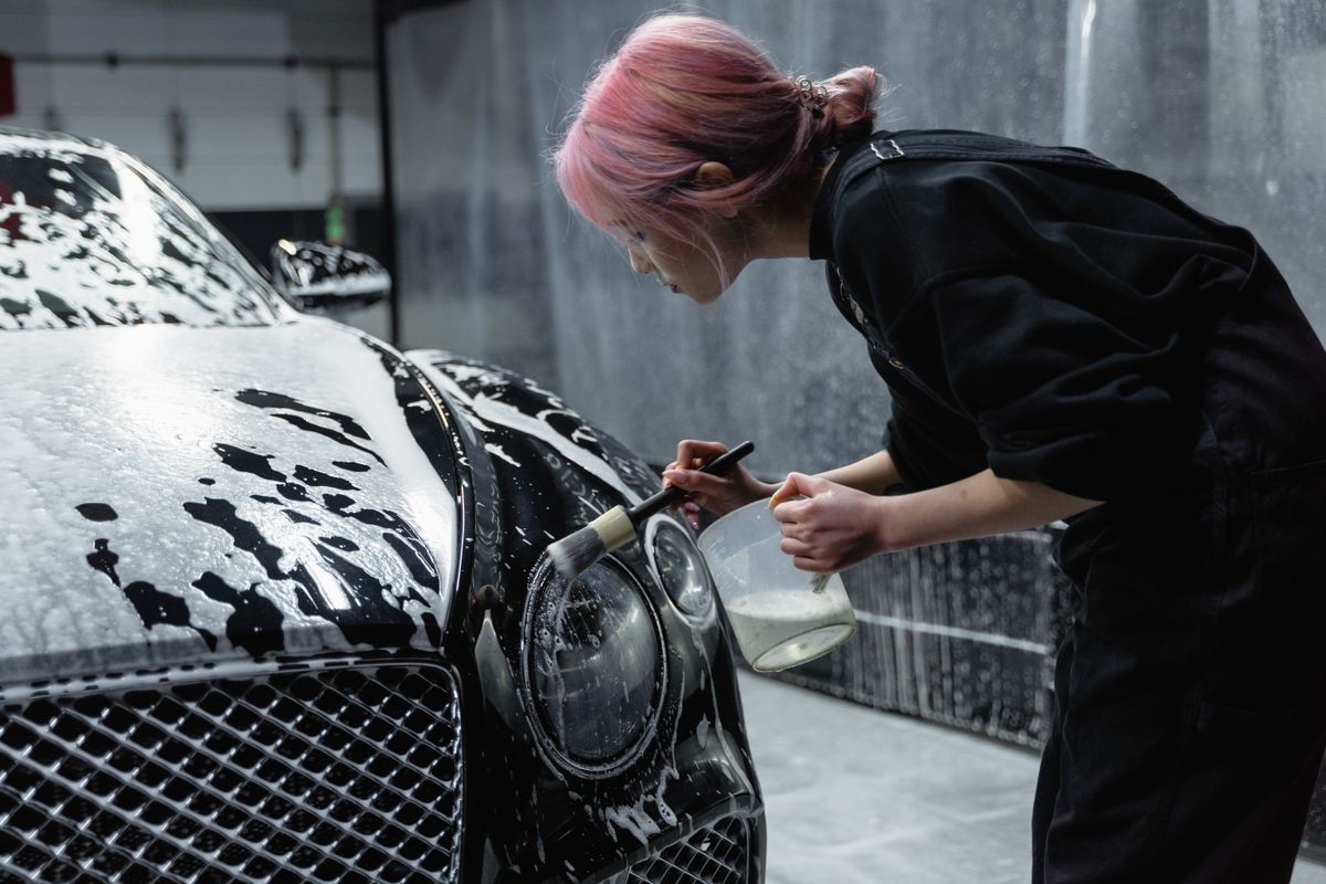 Woman with pink hair brushing the headlight of a black car during a detail