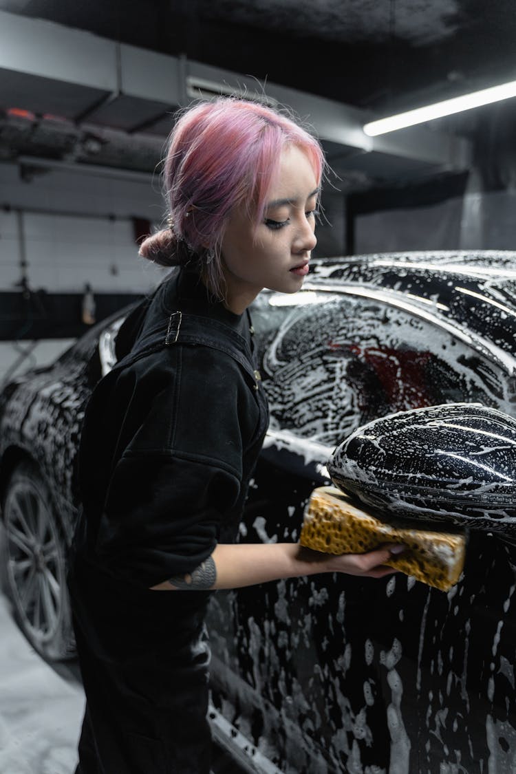 A Woman Cleaning A Black Car Using A Sponge