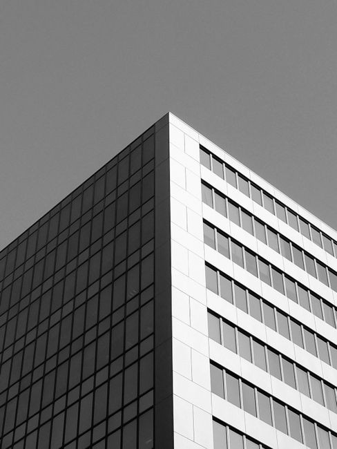 Low angle black and white of corner of modern multistory building with geometric design and symmetric glass windows under cloudless sky on sunny day