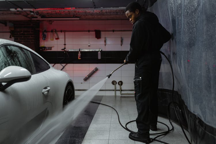 Man In Black Jacket Cleaning The White Car Parked On A Garage