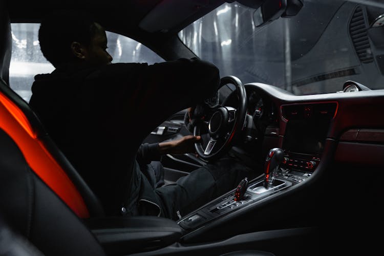 A Man Sitting On The Driver's Seat Wiping The Steering Wheel