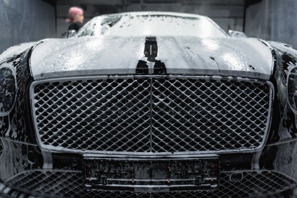 Black car covered in soap foam during a detail wash