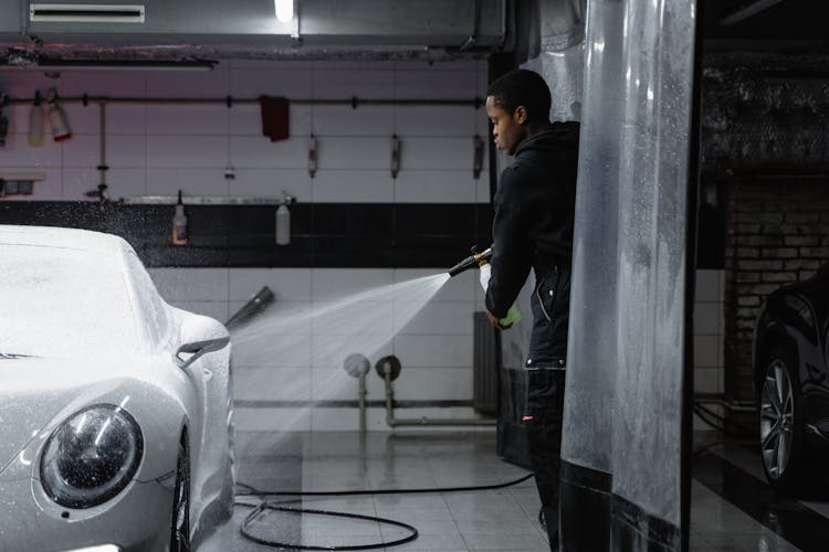 Man In Black Jacket Washing The White Car Using A Washer Pressure Hose