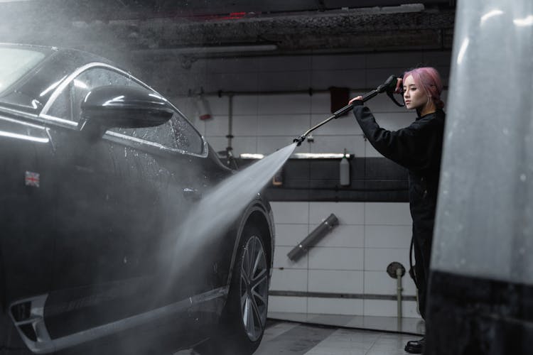 A Woman Cleaning The Black Car Using A Washer Pressure Hose