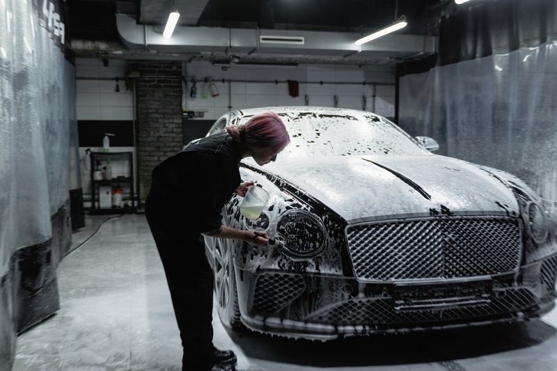 Worker washing a luxury car in a foam-filled garage