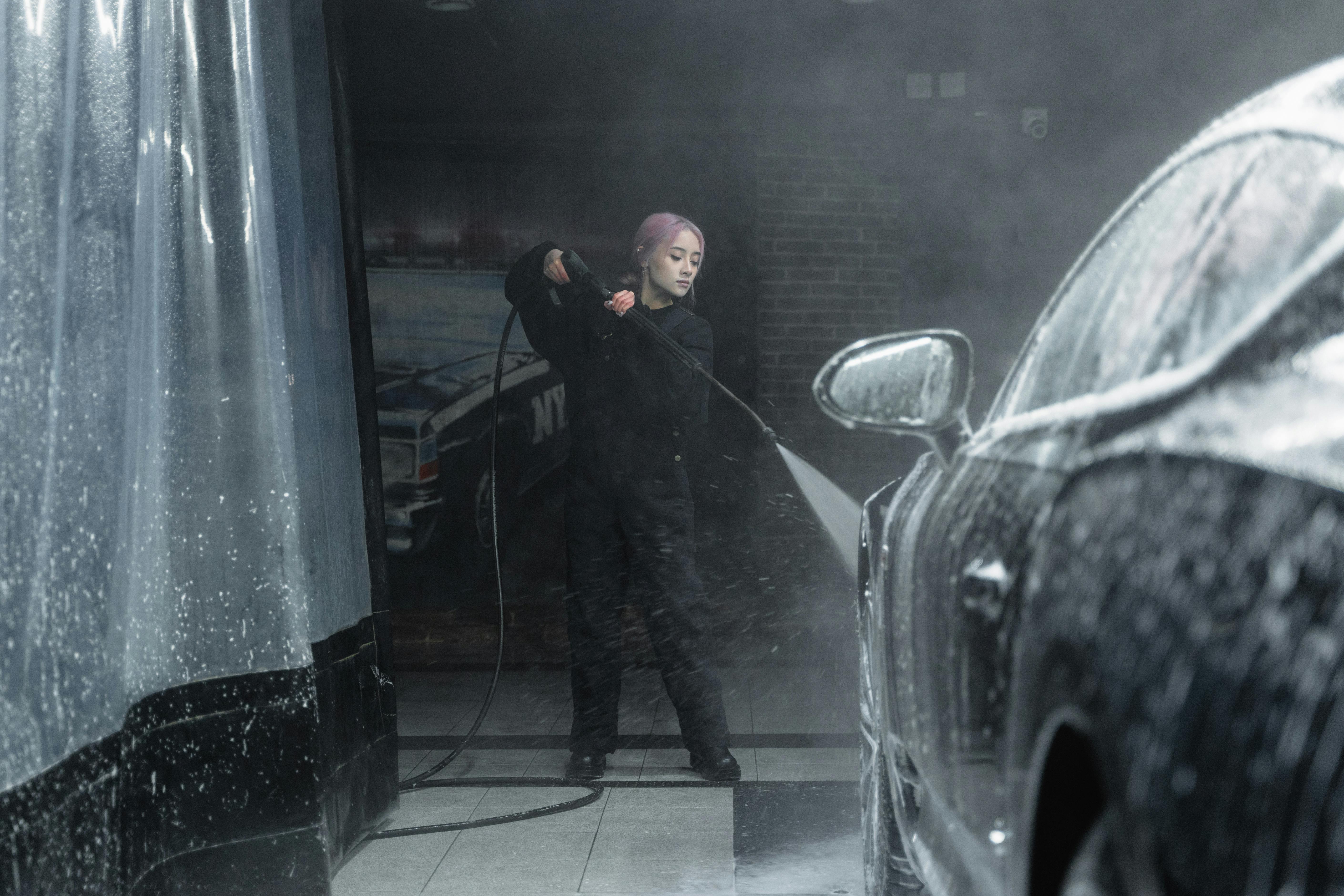 a woman washing a black car using a power spray