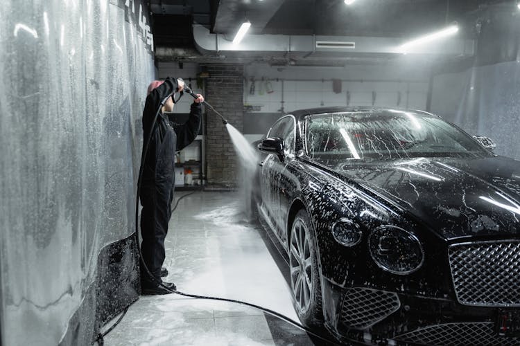 Woman In Black Uniform Washing A Black Car