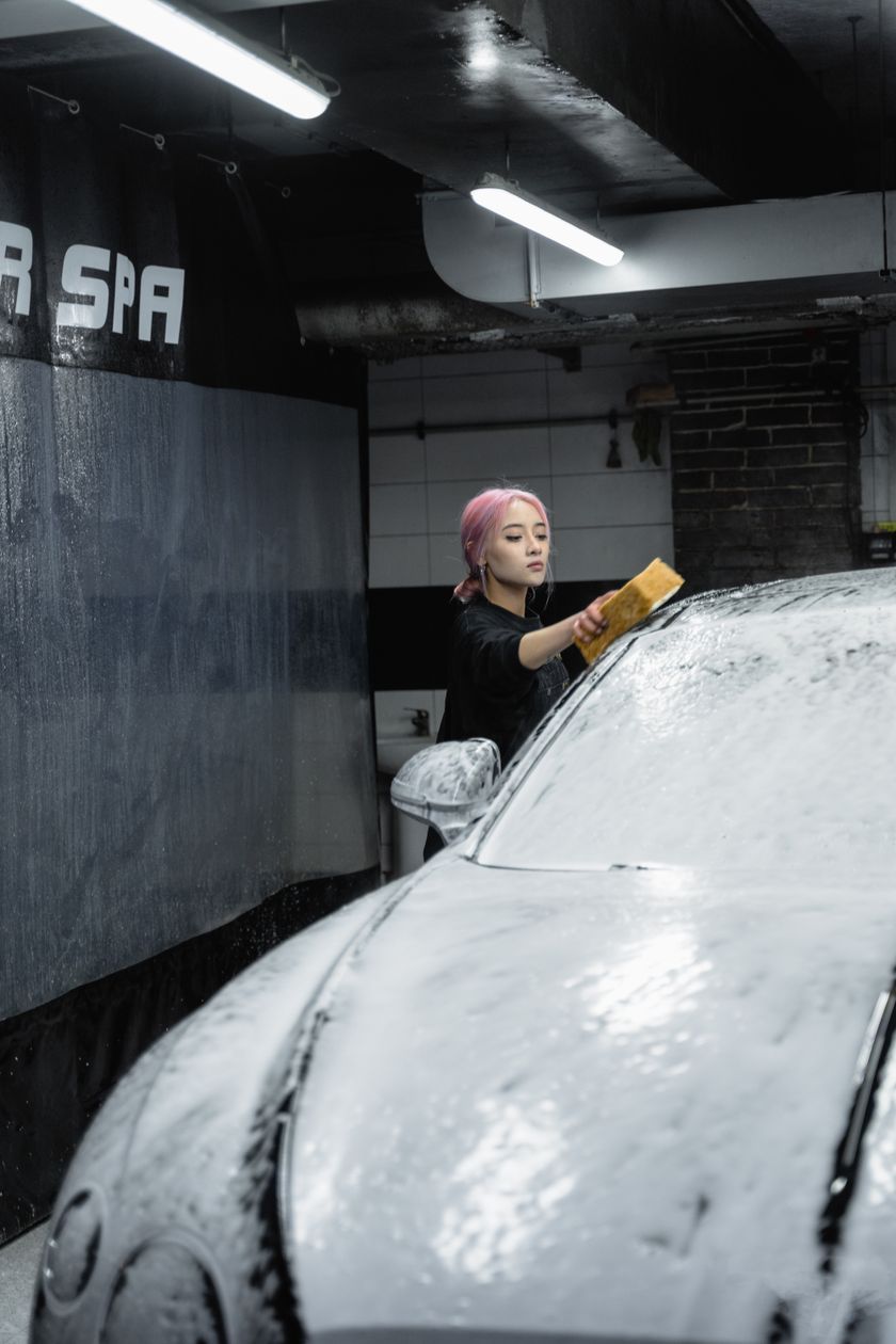 Detailer hand-washing a black car with a sponge and soap