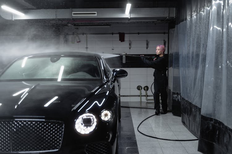 A Woman Washing A Car With A Power Spray