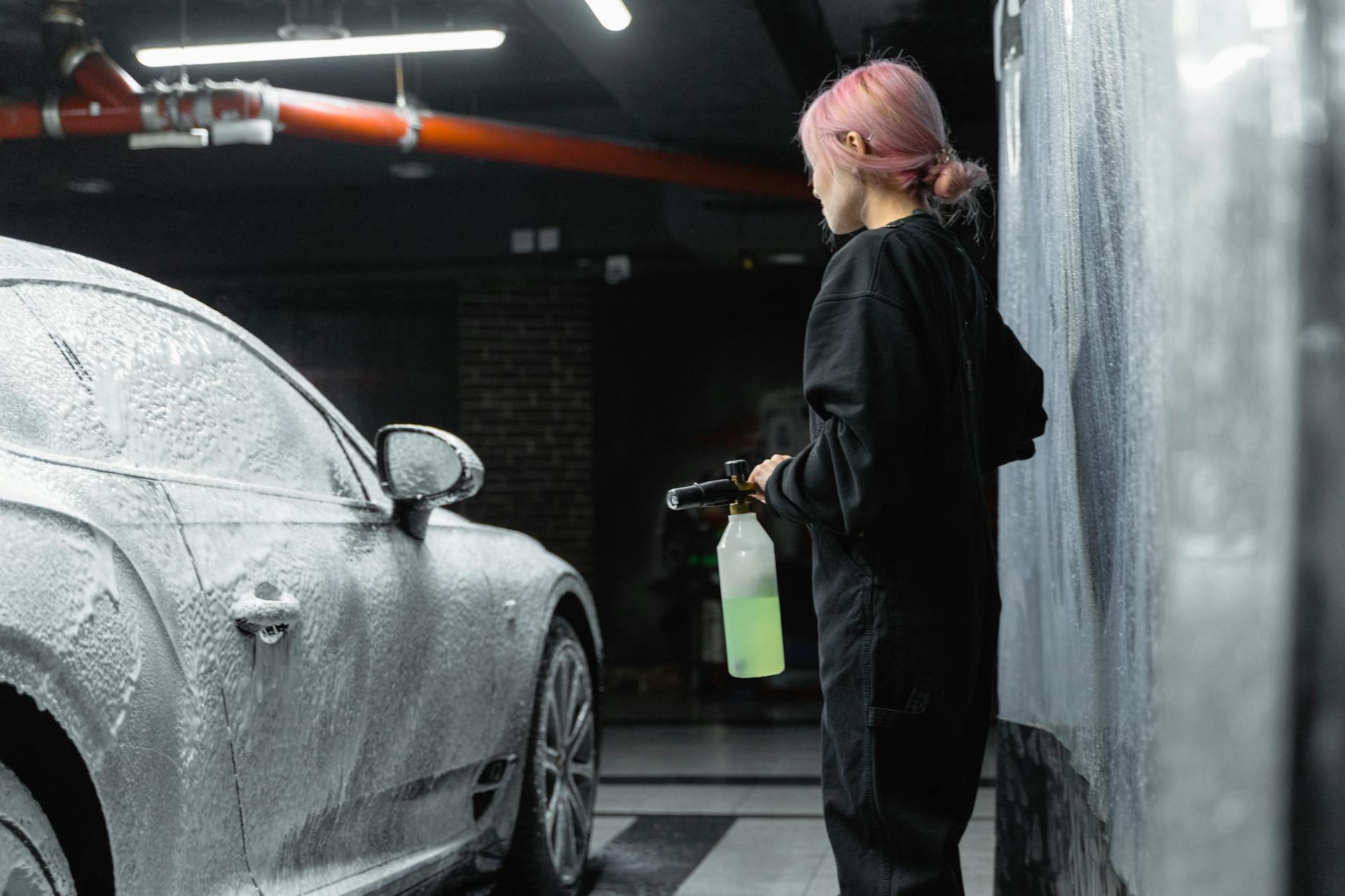 Une femme recouvre une voiture de mousse de shampooing