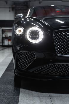 Close-up of a luxury black car's front showcasing its headlights and design in an indoor garage.