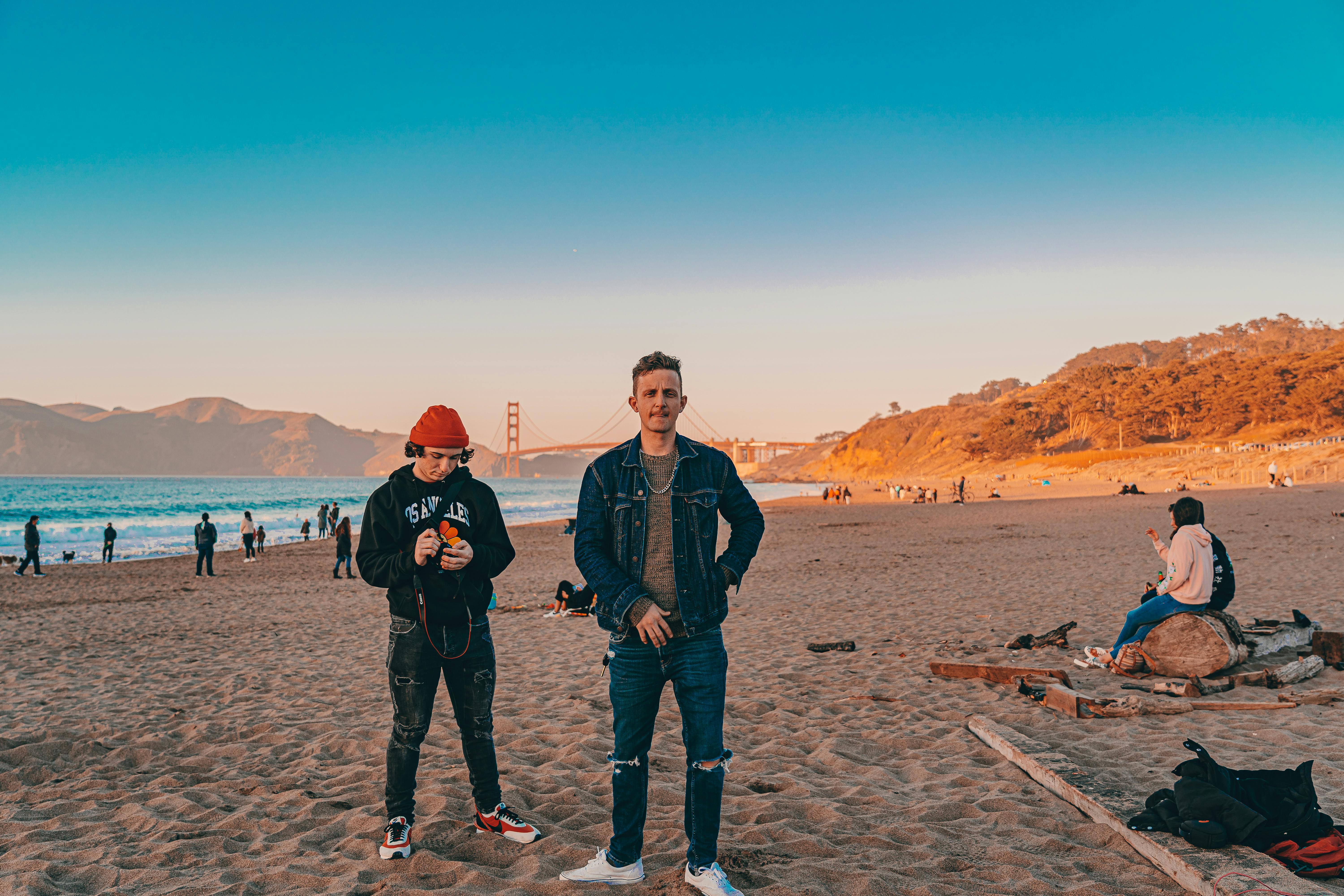 People enjoying a vibrant sunset at a San Francisco beach with the Golden Gate Bridge in view.