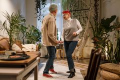 Senior couple dances joyfully in a bohemian home interior filled with indoor plants.