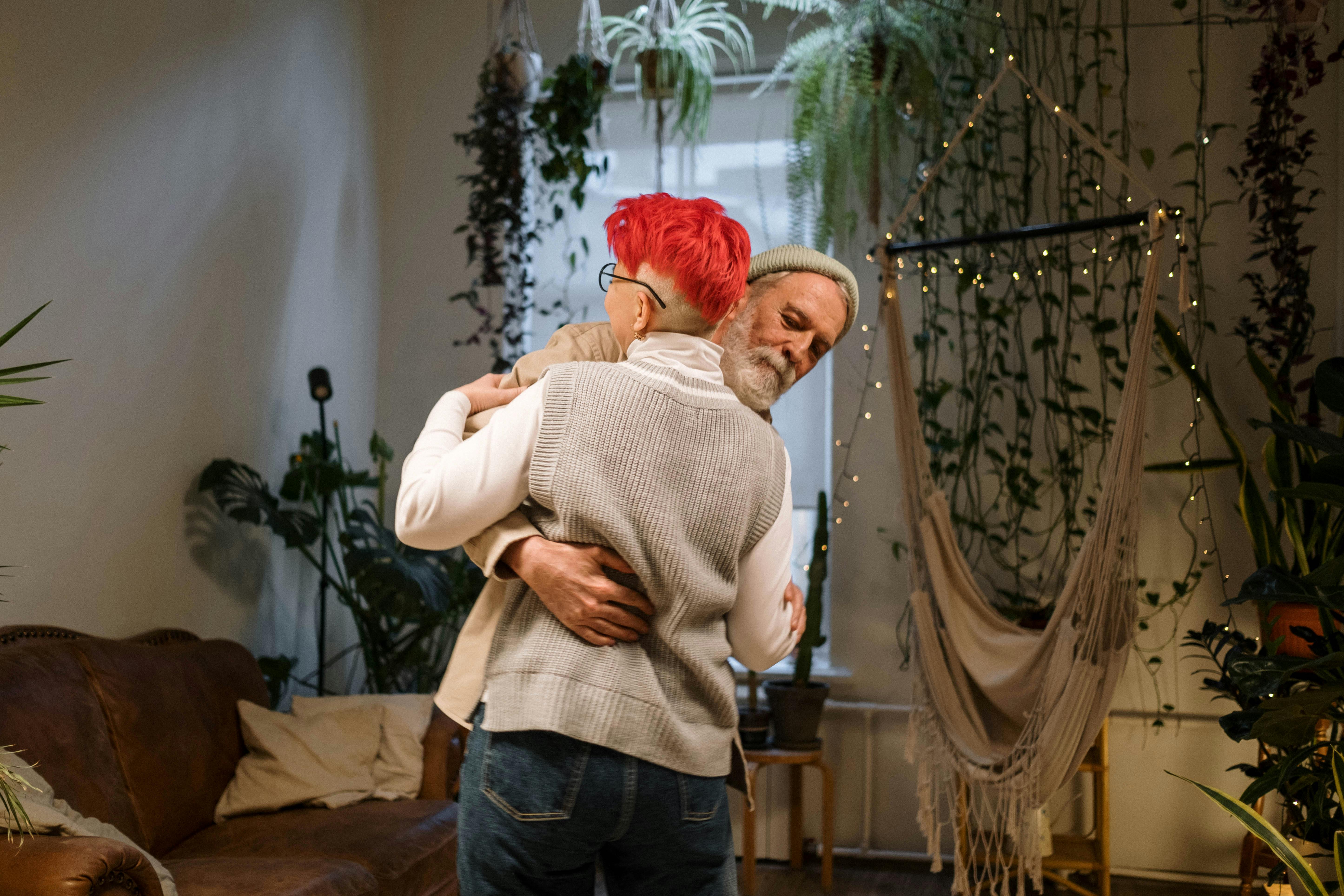 Elderly couple hugging warmly in a lush indoor garden with cozy decor.