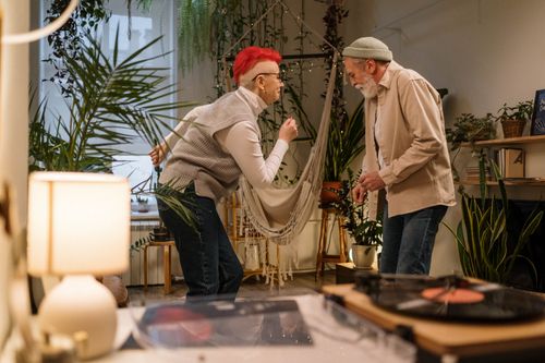 Free An elderly couple joyfully dancing in a cozy, plant-filled living room. Stock Photo
