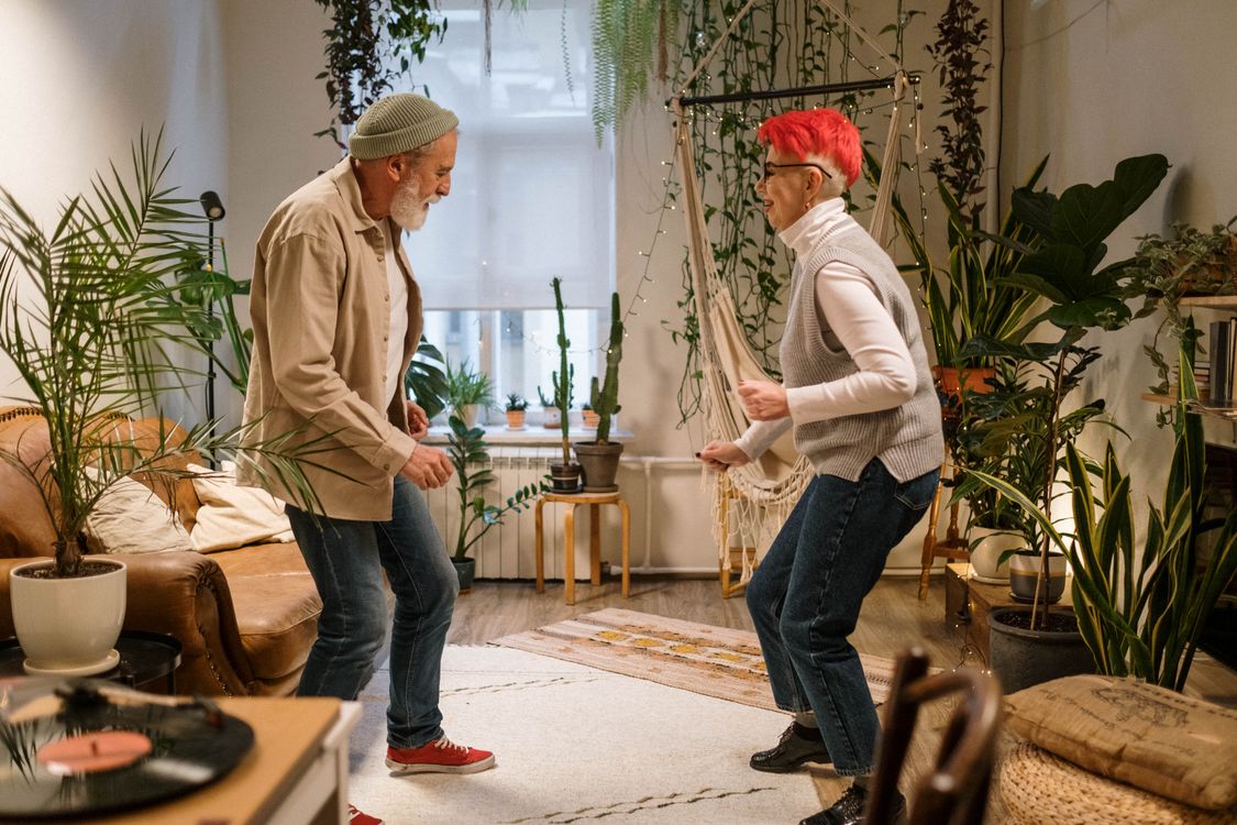 Free Energetic senior couple dancing together at home surrounded by indoor plants. Stock Photo