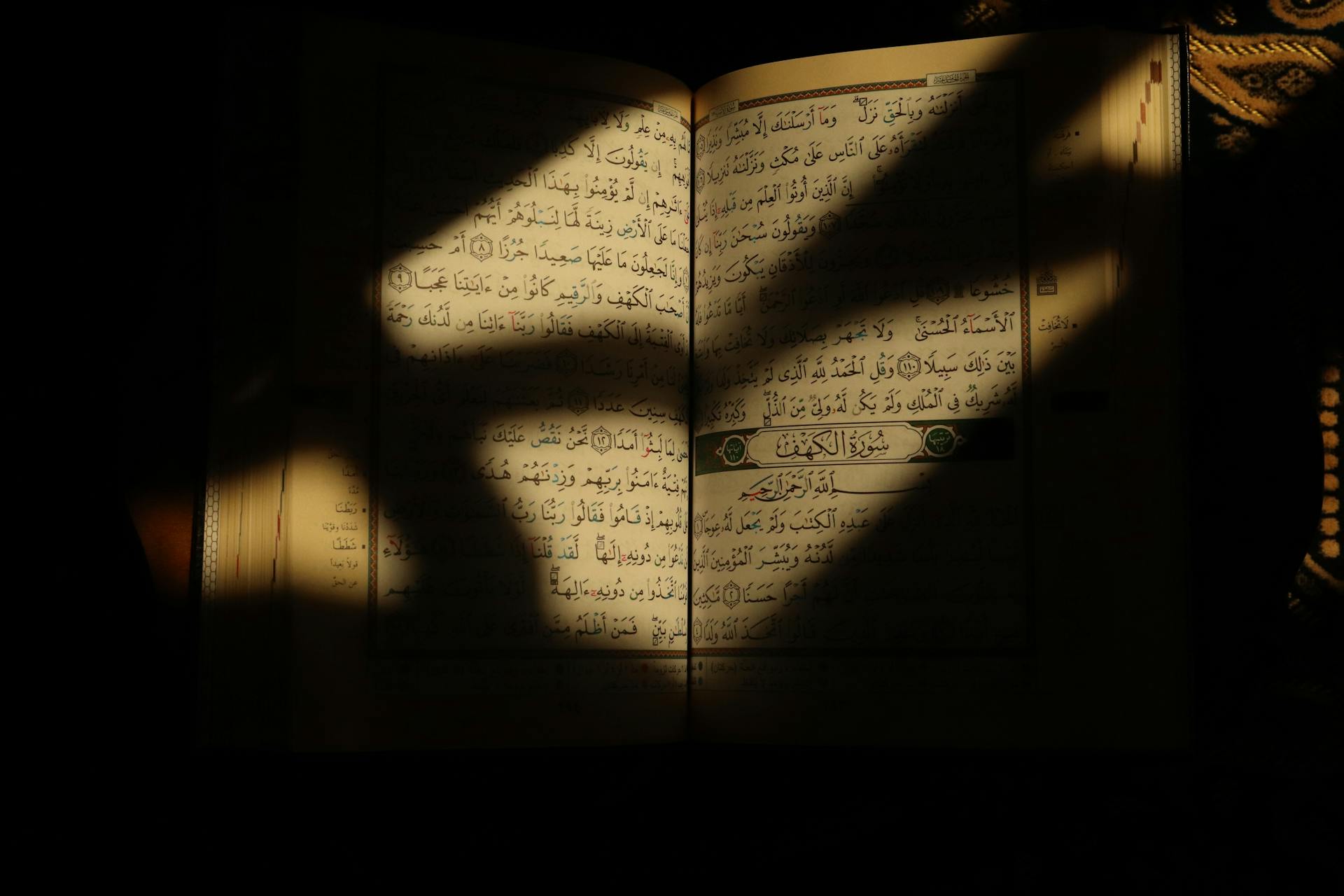 Open Quran with shadows and warm light, emphasizing the holy text in an intimate setting.