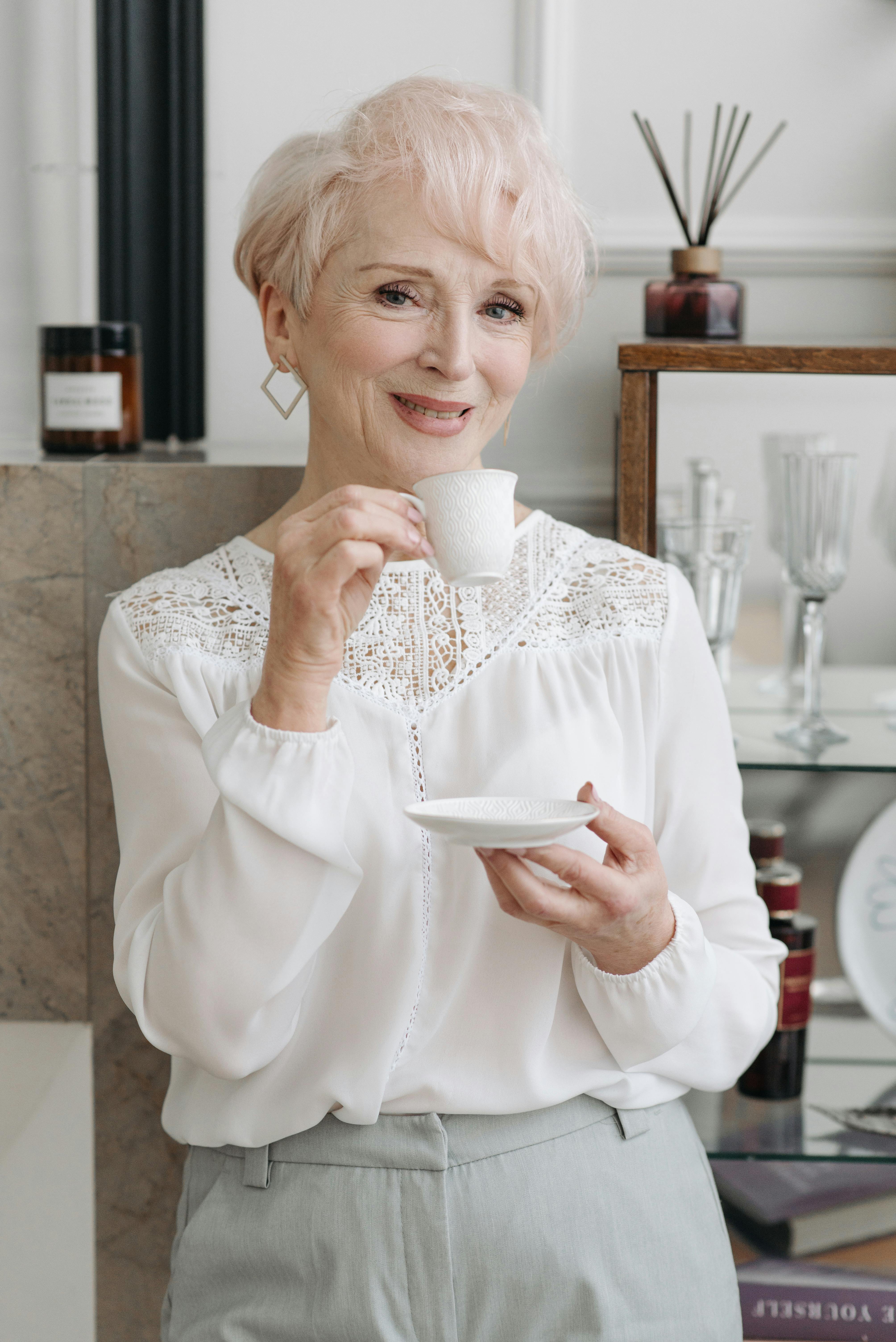 an elderly woman holding a white cup