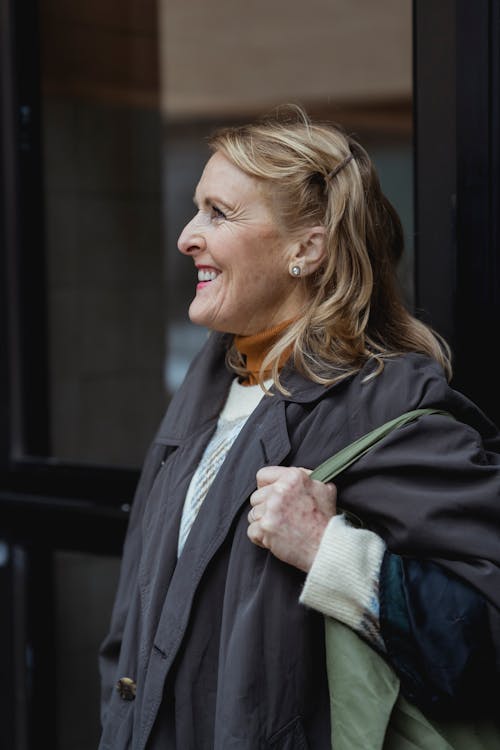 Side view of cheerful middle aged female in coat and with curly hair looking away in daytime