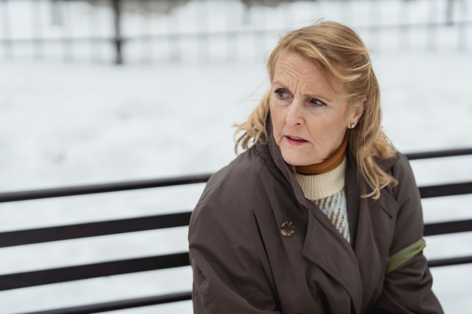 Contemplative elderly female with wrinkled skin in outerwear looking away while resting on urban bench in wintertime