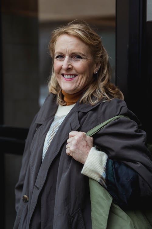 Free Content senior female in coat with bag and blond hair looking at camera in daytime Stock Photo