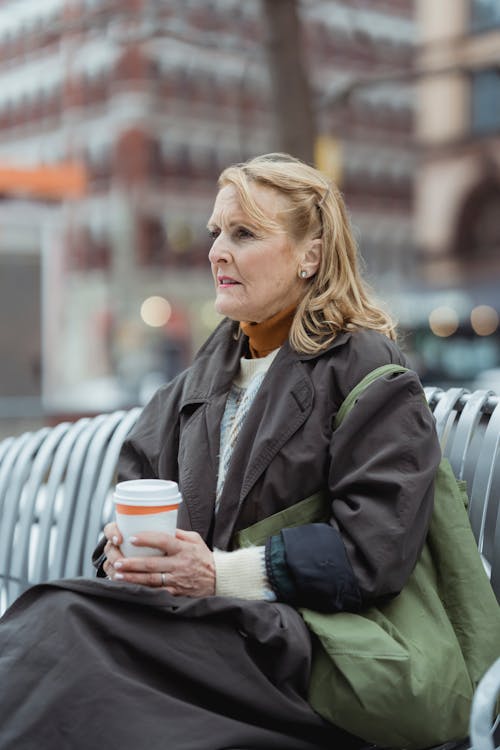 Elderly woman with disposable cup of coffee on urban bench