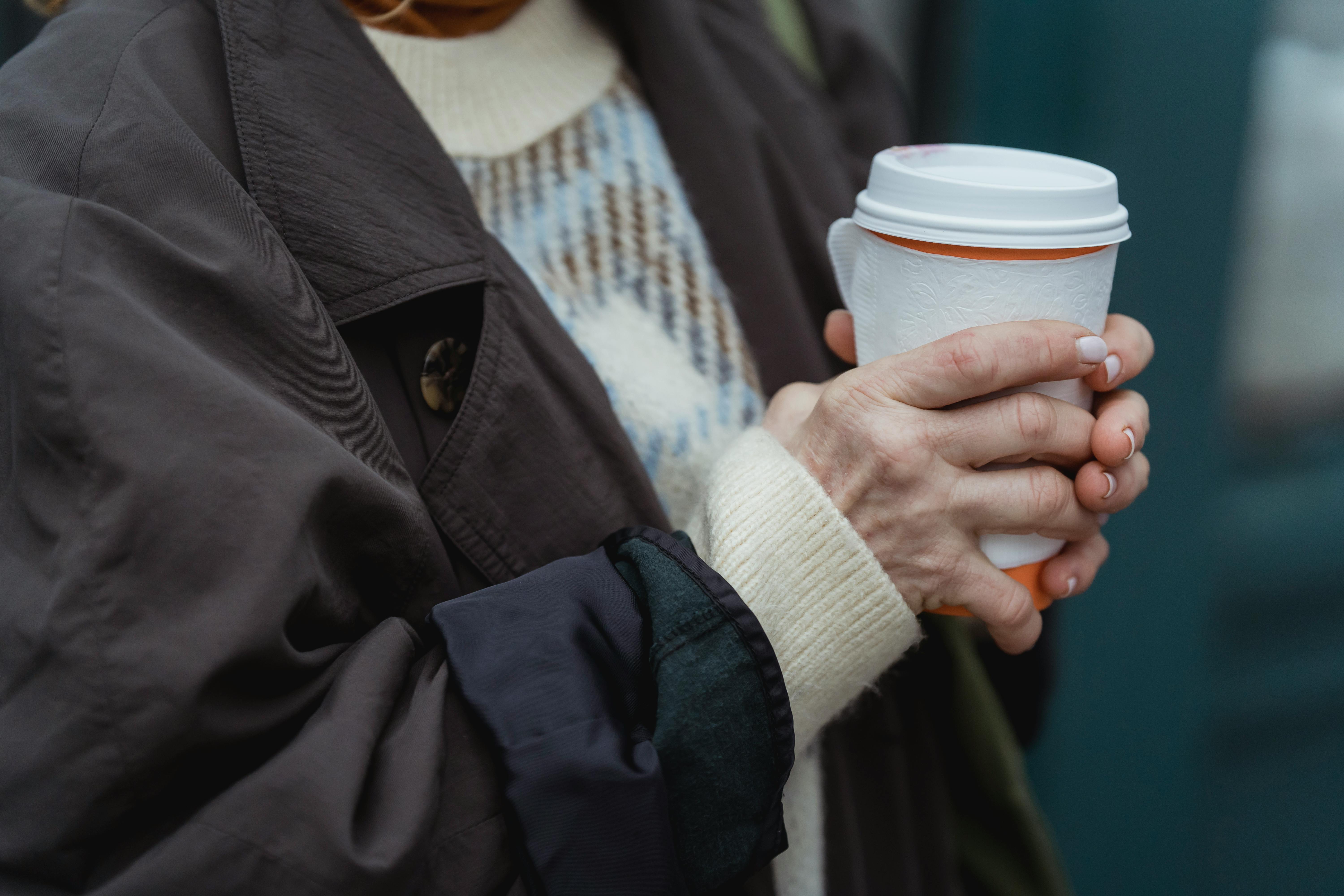 Close-up of a woman holding a takeaway coffee cup outdoors, wearing winter clothing.