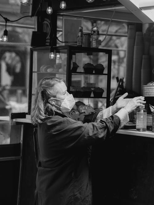 Free Black and white side view of elderly female customer in protective mask applying antibacterial gel at counter in bakery Stock Photo