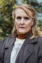 Senior female with wrinkled face skin and blond hair in warm clothes looking at camera outdoors