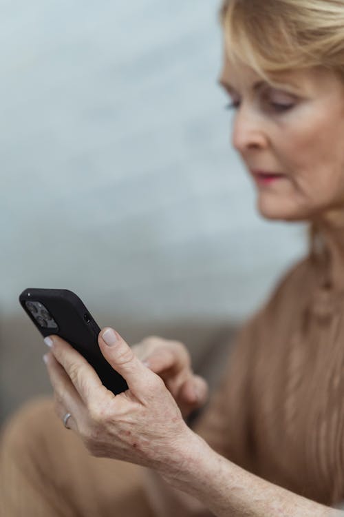 Crop senior woman chatting on smartphone at home