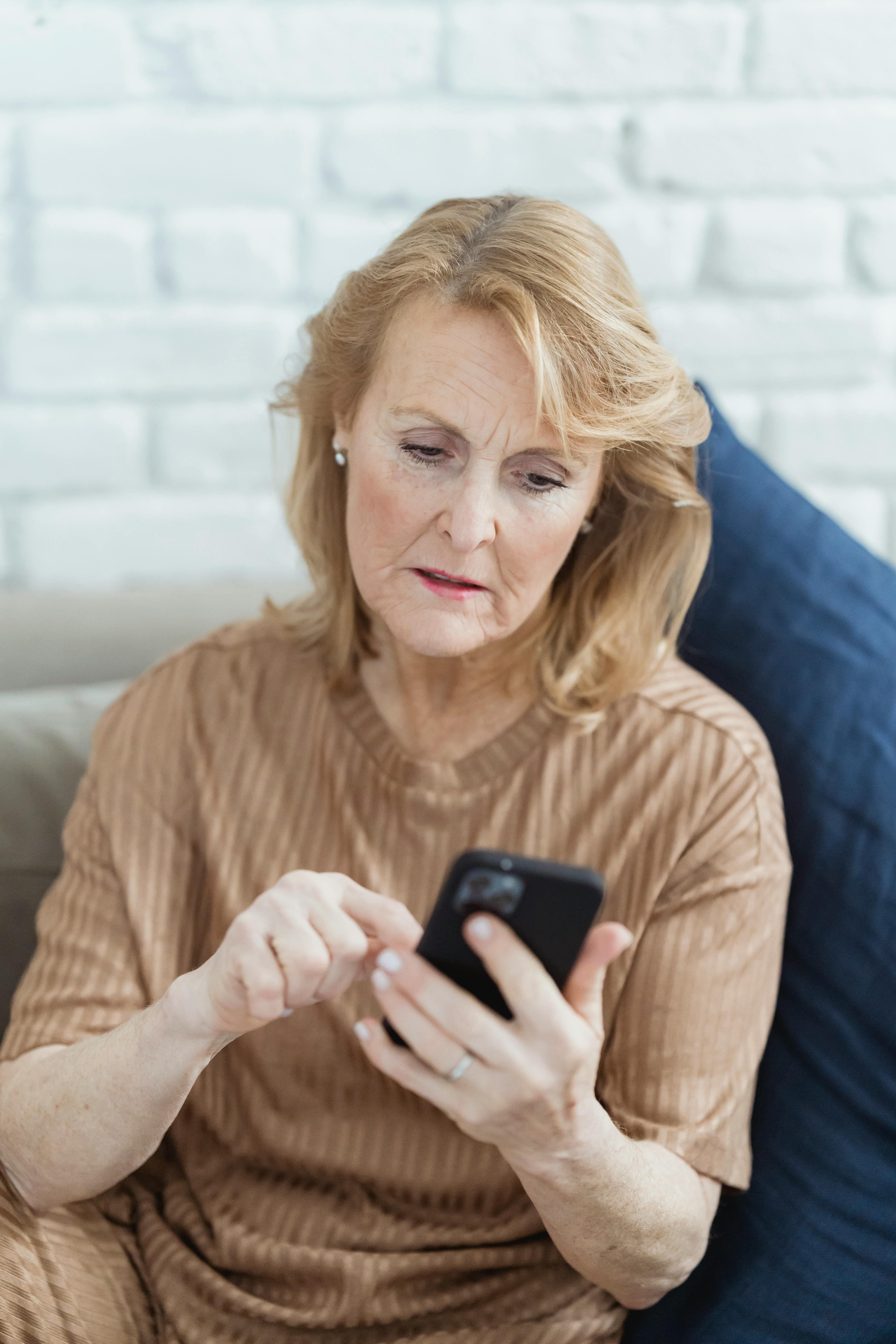 elderly woman chatting on smartphone on sofa at home